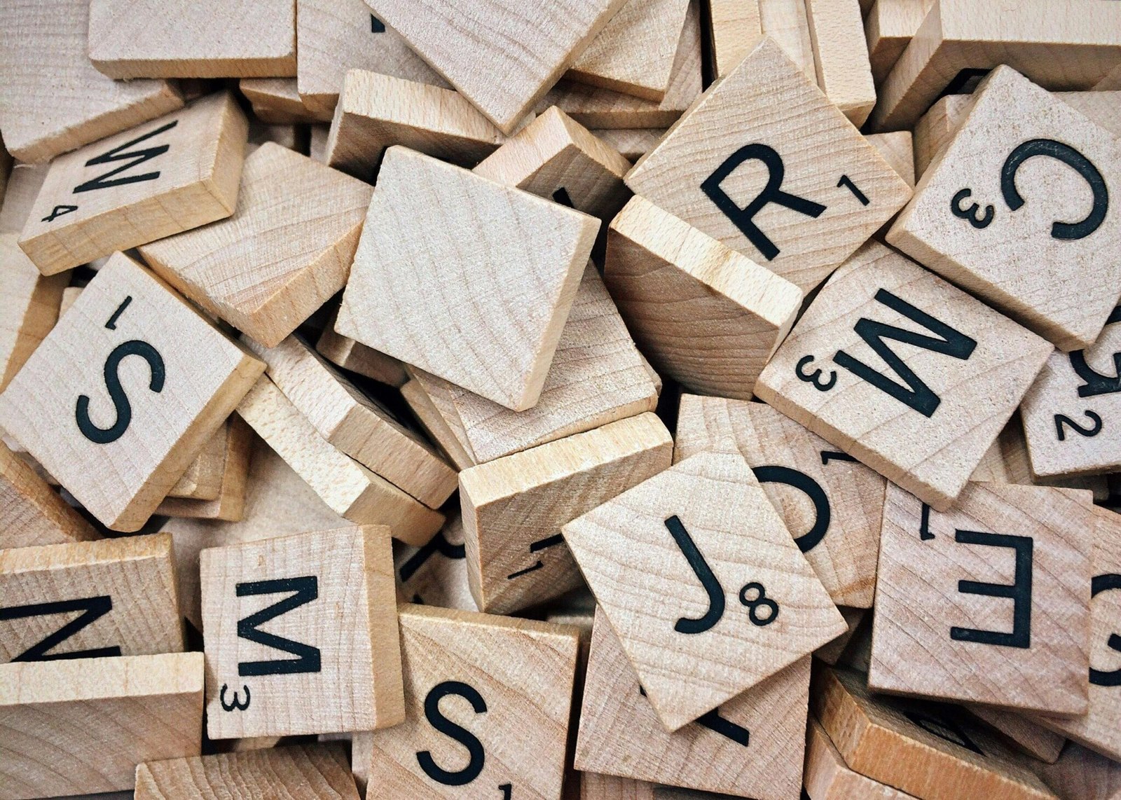 Juego de palabras con letras de madera - Solidaritas Piezas de madera con letras y números de un juego de palabras, apiladas en un montón.