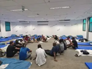 Grupo de homens sentados em um círculo em uma sala com colchões no chão.