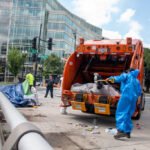 Caminhão de lixo laranja realizando a coleta de resíduos em uma área urbana.
