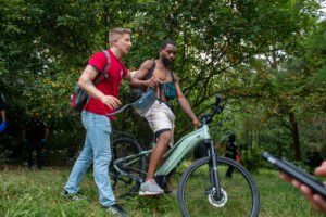 Um homem em uma bicicleta elétrica sendo ajudado por outra pessoa em um ambiente natural.