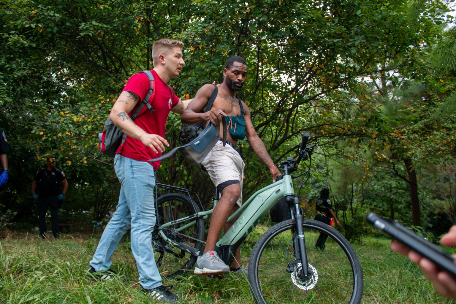 Um homem em uma bicicleta elétrica sendo ajudado por outra pessoa em um ambiente natural.