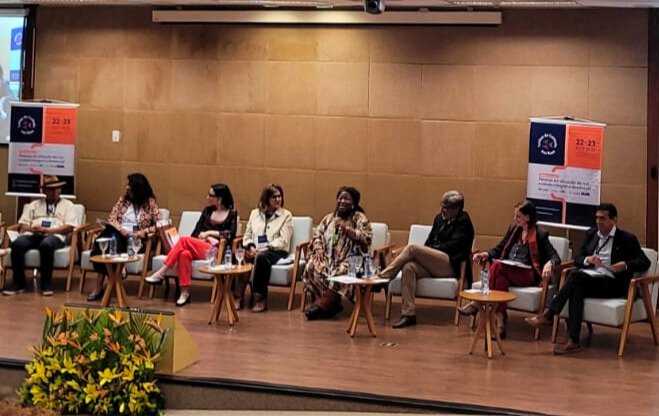 Grupo de pessoas sentadas em um painel de discussão durante um evento em um auditório.