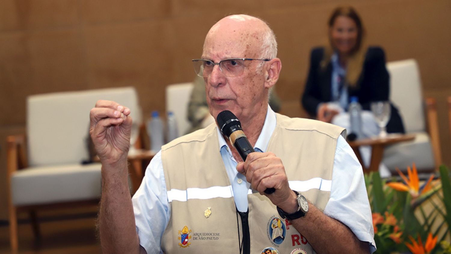 Pe. Lancellotti usando um colete claro e segurando um microfone durante uma apresentação em um evento.